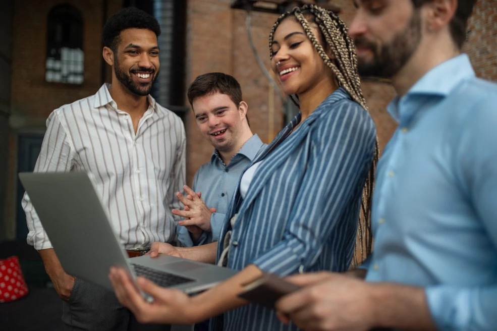 A disabled boy and his coworkers smiling while looking at a laptop
