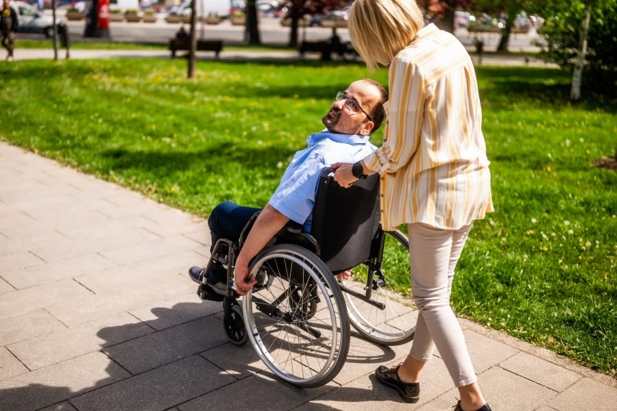 A disabled man sitting in his wheelchair while his support worker walks with him at the park